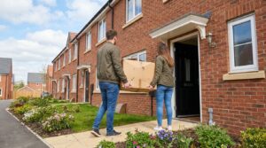 A couple seen from behind carrying a box into a new-build terraced house